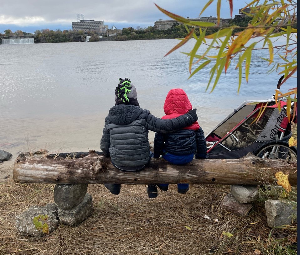 two kids sitting by water looking at waterfall in the distance